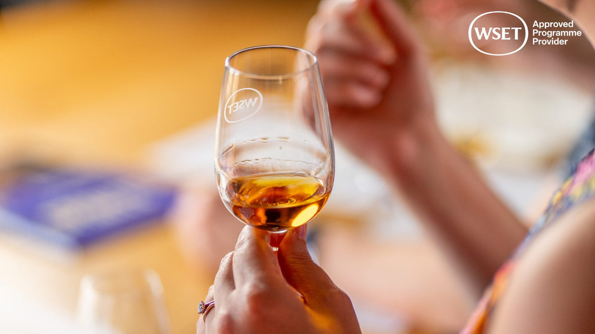 Hand holding a WSET-branded tasting glass of amber spirit during a professional tasting