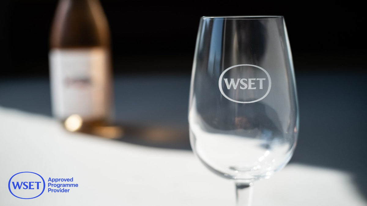 Empty WSET logo tasting glass on a white surface with soft bottle bokeh