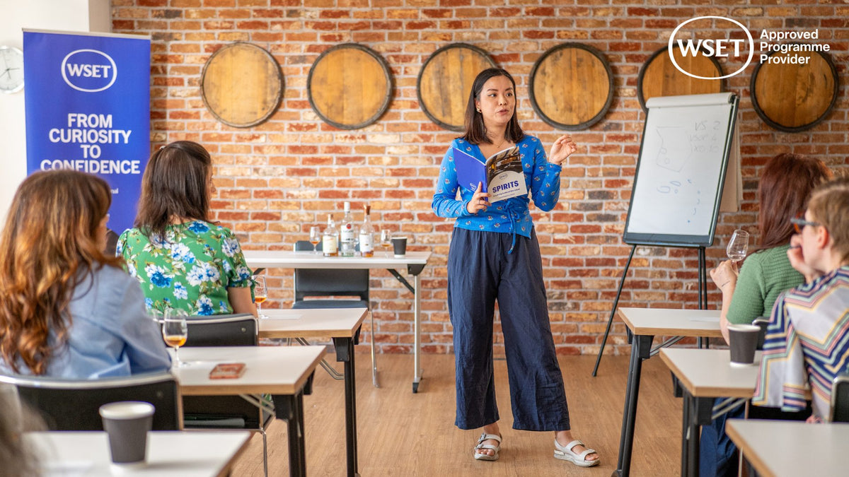 WSET spirits educator teaching a classroom of students with tasting glasses and barrel-end wall decor