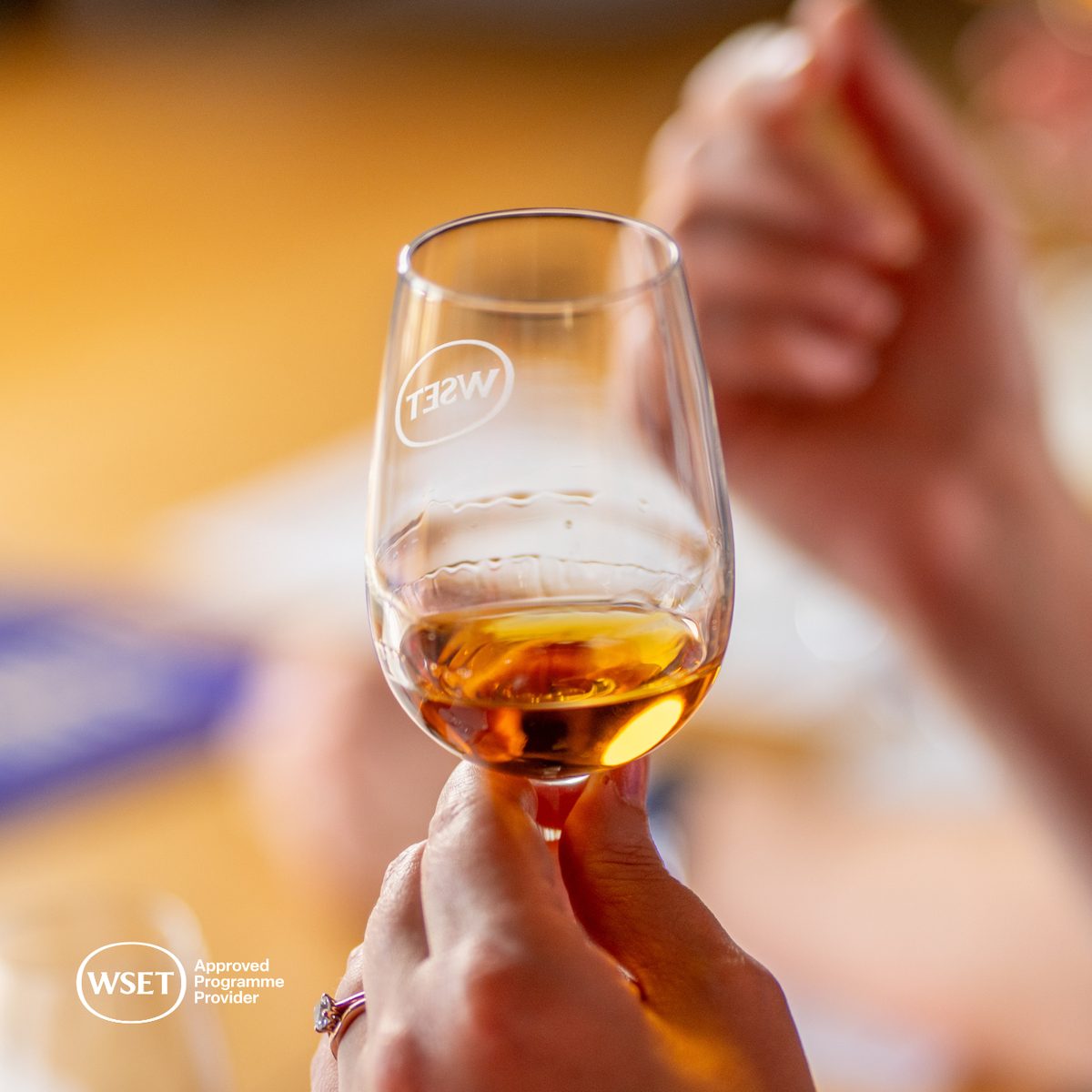 Hand holding a WSET tasting glass of deep amber spirit for colour assessment